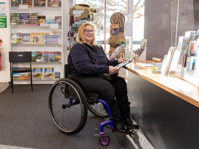 Smiling woman in wheelchair holding a brochure at a visitor information centre